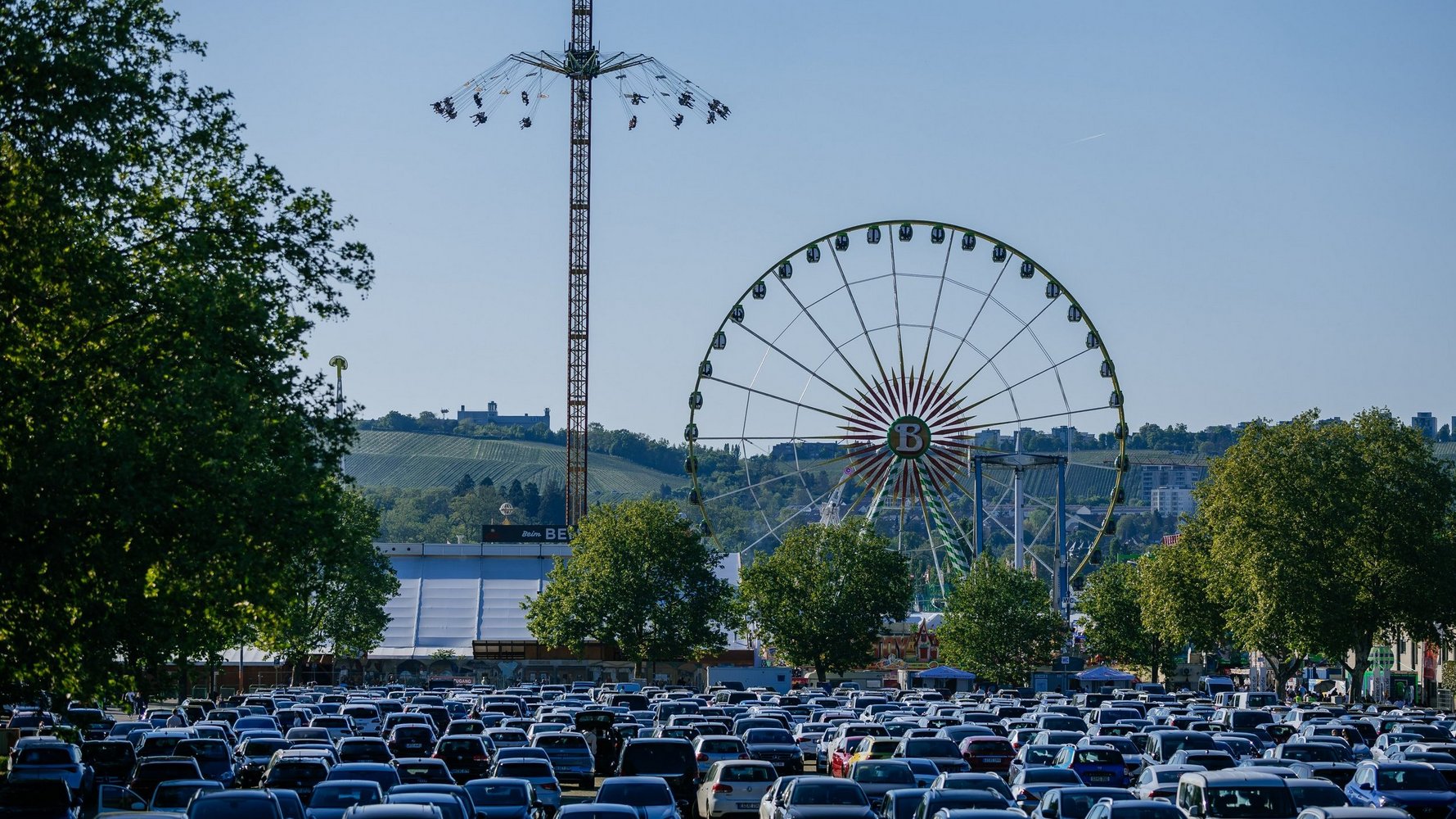 Many cars in the Wasen car park, behind them you can see a chain carousel and the ferris wheel.