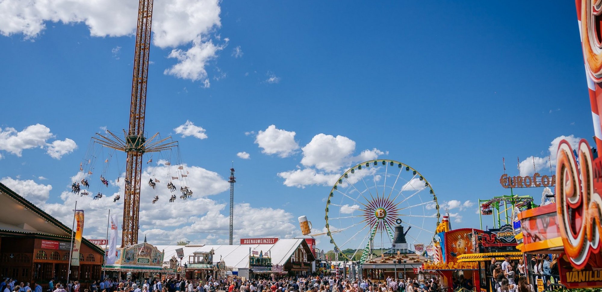 Blick auf den Festplatz mit den Zelten auf der linken Seite. Weiter vorne steht der Info-Pavillon mit der Cannstatter Kanne. Im Hintergrund ist das Riesenrad und der Kettenflieger Aeronaut.