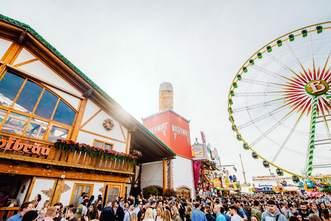 Das Festzelt Wasenwirt von außen. Zahlreiche Menschen stehen davor. Unverkennbares Markenzeichen ist der Maßkrug auf em Turm neben dem Zelt.