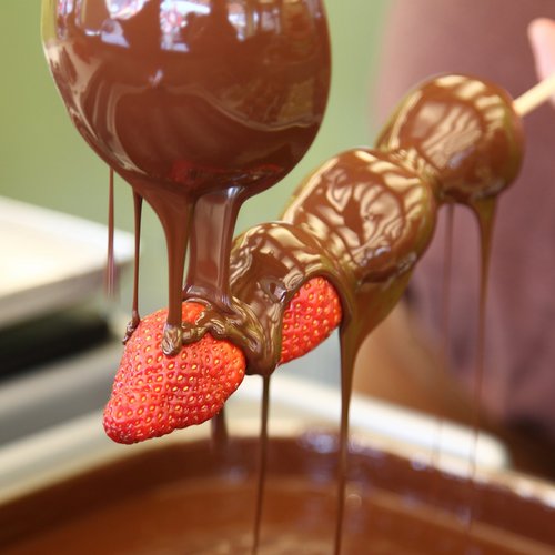 Erdbeeren werden an einem Spieß mit einem Löffel heißer Schokolade überzogen