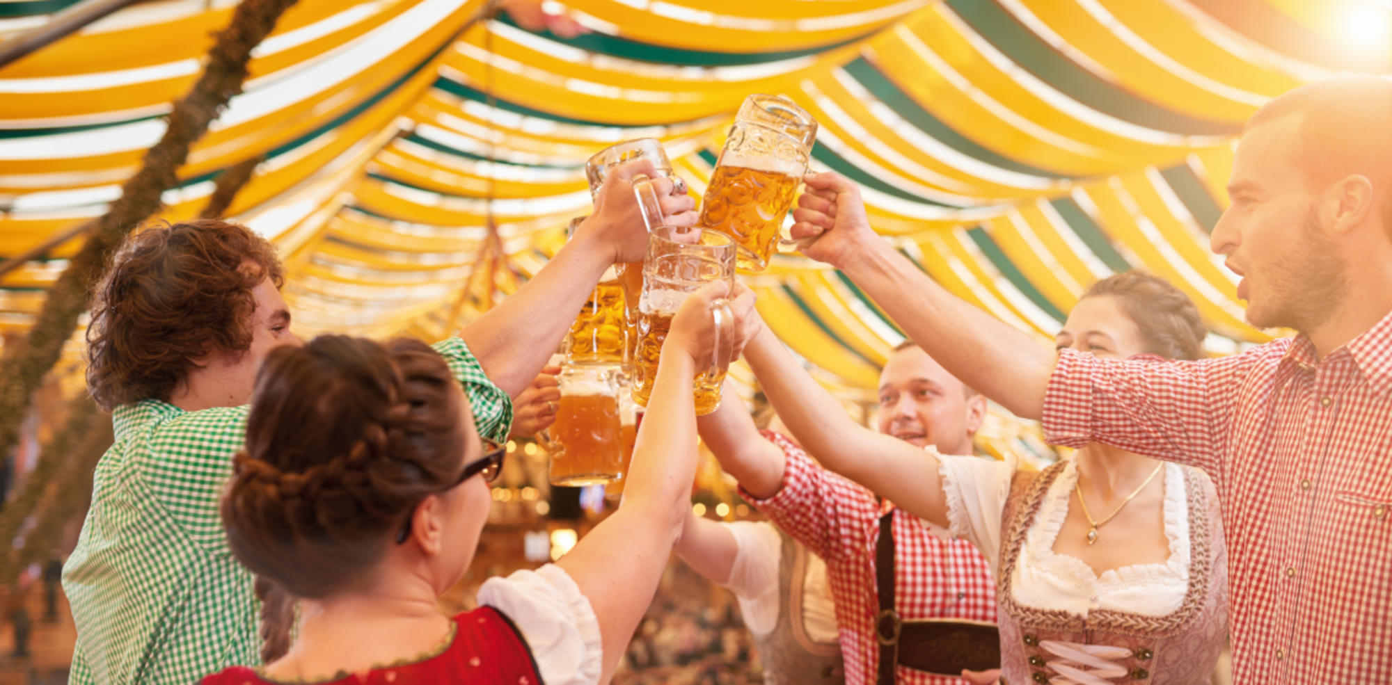 Männer und Frauen, die in einem Fetzelt auf einer Bierbank stehen und mit Bierkrügen anstoßen. 