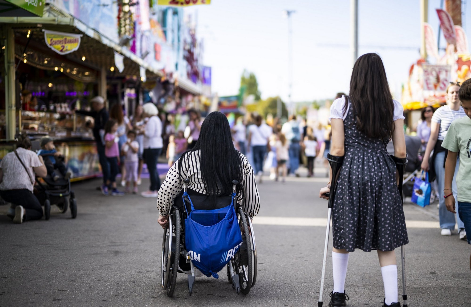 Eine Frau im Rollstuhl und eine an Krüken sind auf dem Wasen unterwegs.