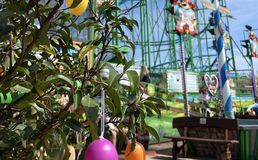 Im Vordergrund ist ein mit bunten Eiern geschmückter Strauch zu sehen, im Hintergrund ein Fahrgeschäft des Frühlingsfestes.