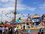 Blick auf Aeronaut- und Shake-Karussell vor blauem Himmel. Im Vordergrund Besucherinnen und Besucher.