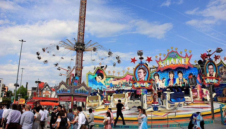 Blick auf Aeronaut- und Shake-Karussell vor blauem Himmel. Im Vordergrund Besucherinnen und Besucher.