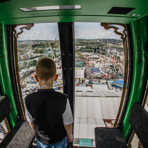 Ein Junge steht in einer Gondel des Riesenrads und blickt auf das bunte Treiben unter ihm.