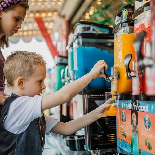 Ein Junge, der mit einen Becher mit gelbem Slush-Eis aus einer Maschine füllt.