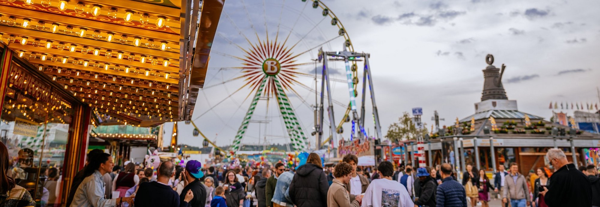 Frühlingsfest in der Dämmerung, im Hintergrund das Riesenrad und das Info-Pavillon mit der Cannstatter Kanne.